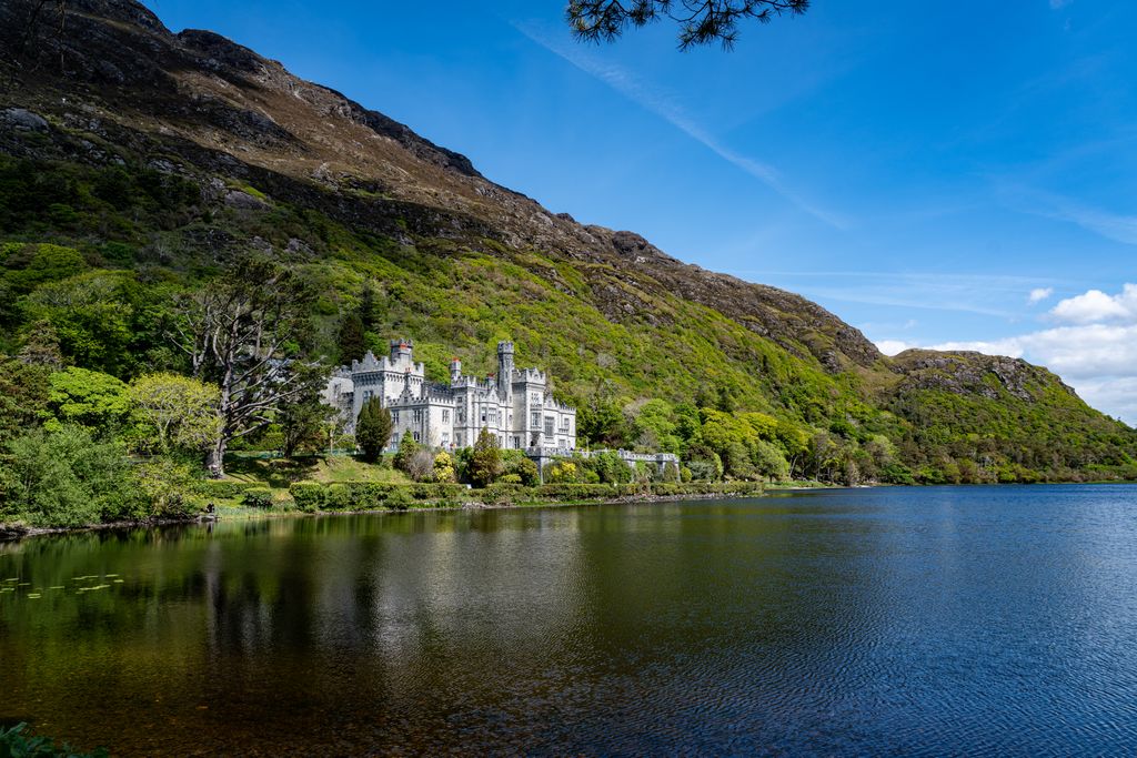 A picturesque view of Kylemore Abbey by the lake in lush greenery.