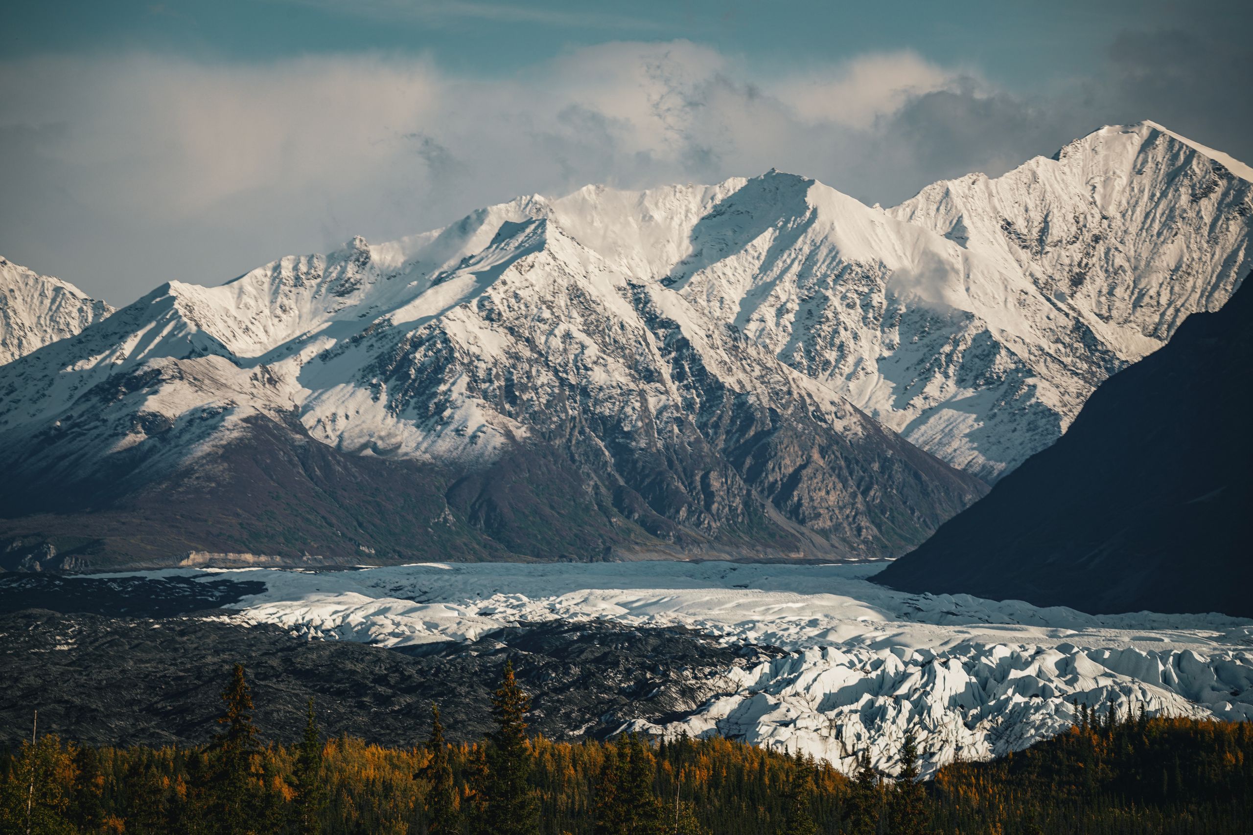 Breathtaking view of snow-capped mountains with a glacier below, captured in serene winter light.